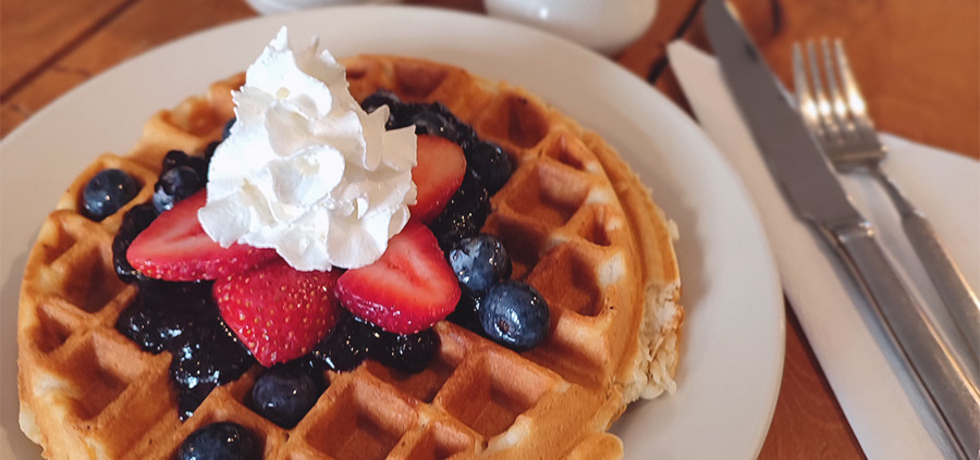 An upclose image of a waffle, drizzled with house bourbon fruit compote, fresh whipped cream, and fresh fruits.